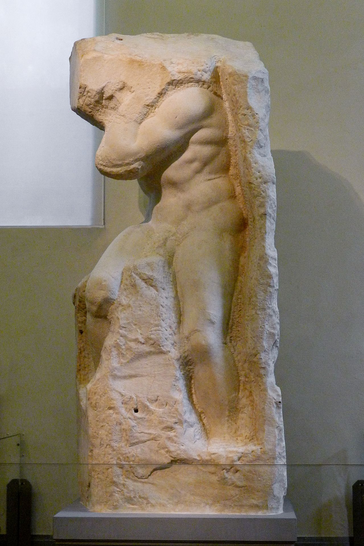 An unfinished marble sculpture — a powerful figure partially emerging from raw stone, the form persisting where the chisel stopped, dissolving where it did not